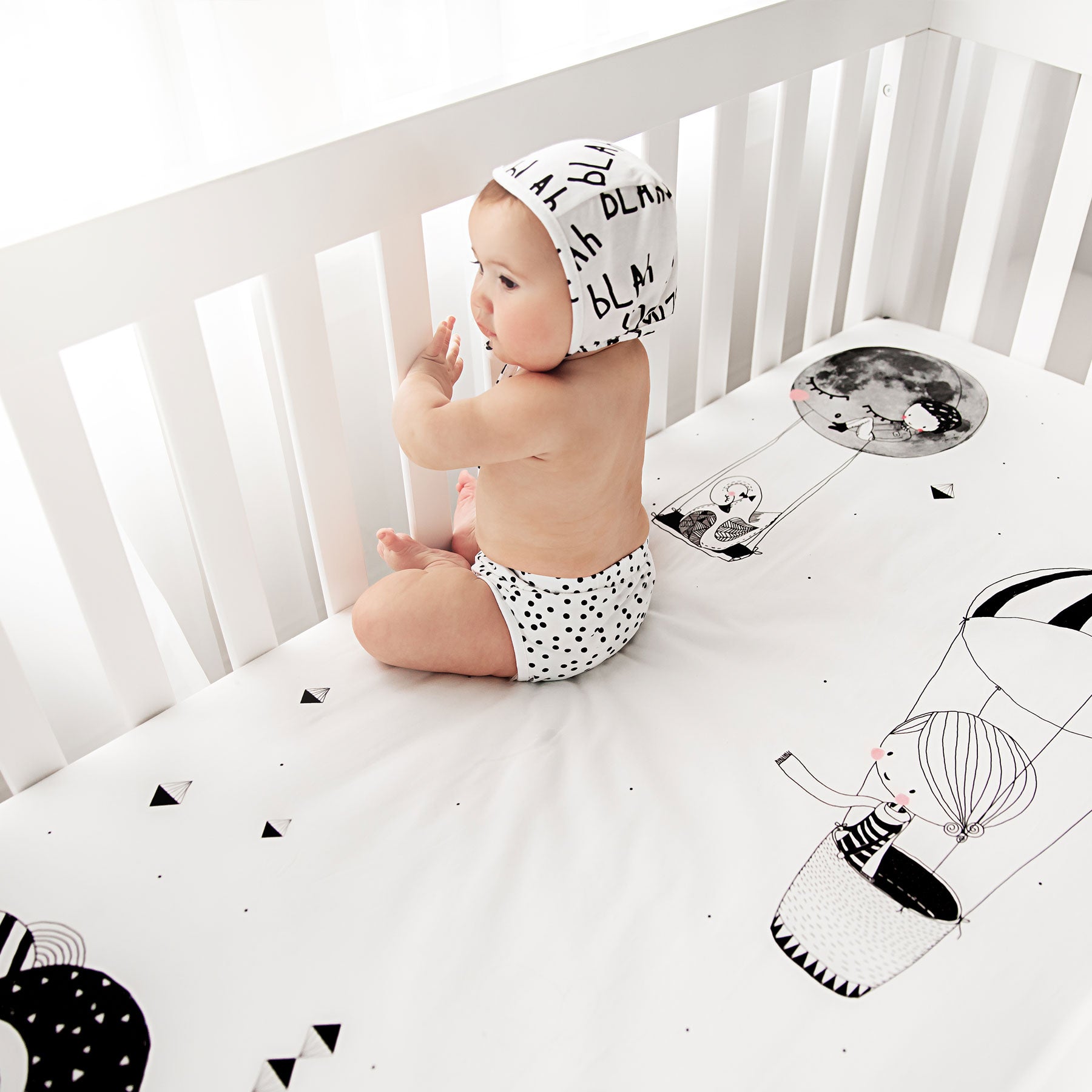 Fitted baby crib sheet by Rookie Humans, Frieda and the hot air balloon. Illustrated by Swanjte Hinrichsen. Designed for the modern nursery, packaged to make a unique baby shower gift. Monochrome nursery.